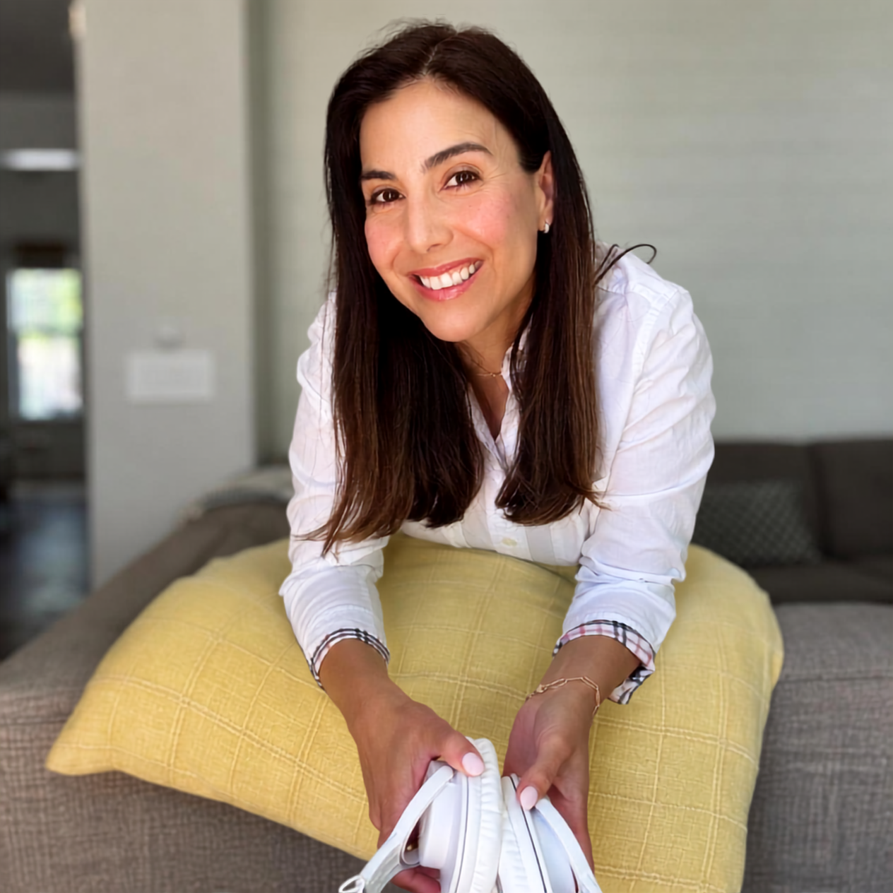 Camille smiling on the couch, holding white headphones