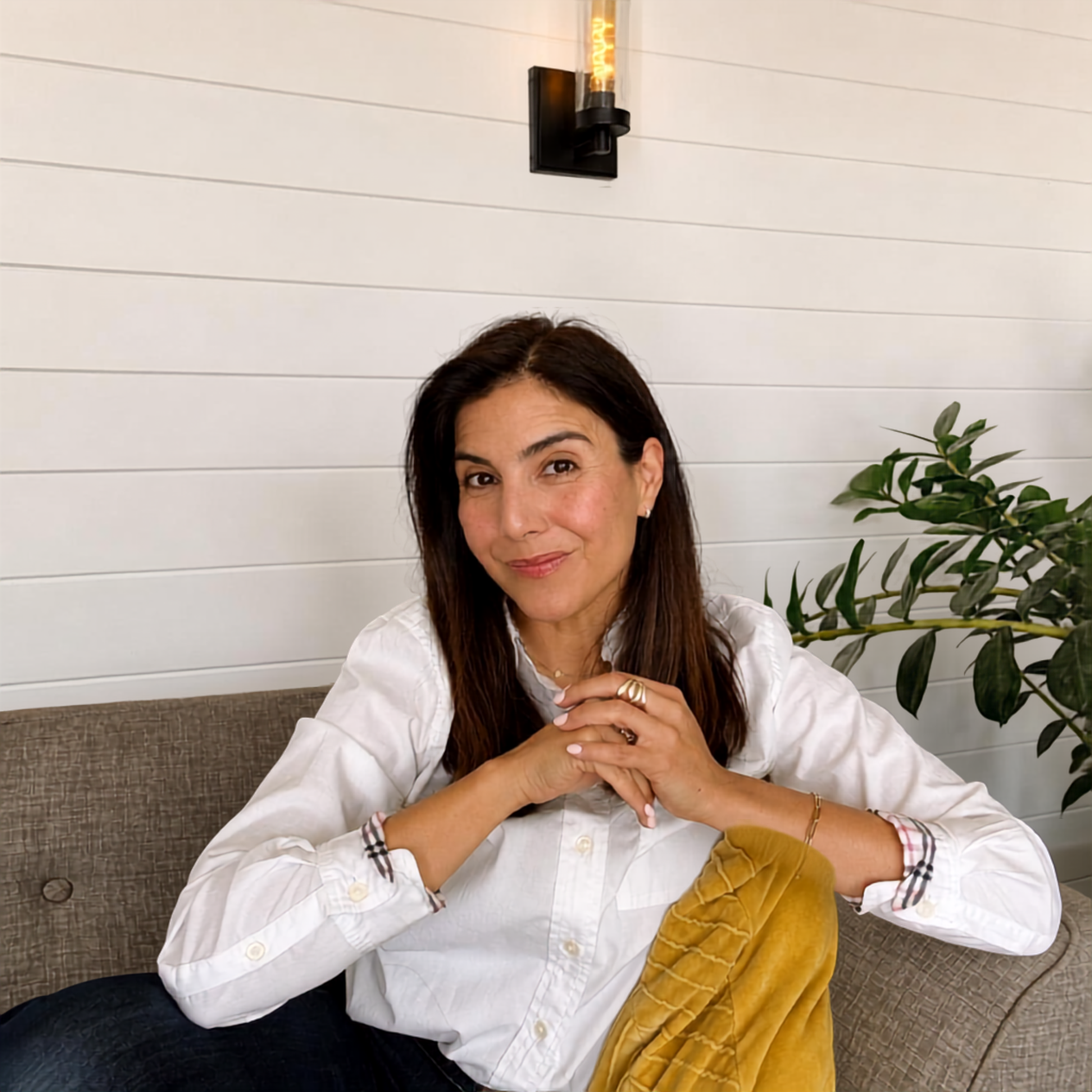 Camille seated on a sofa with her hands clasped, smiling